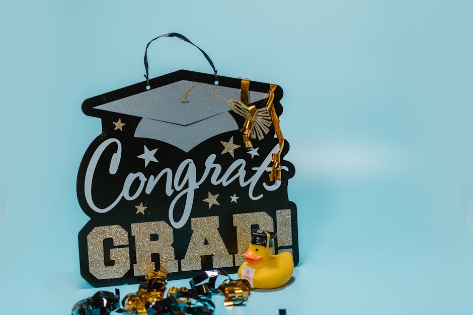 Festive graduation sign with mortarboard and a rubber duck on light blue background.